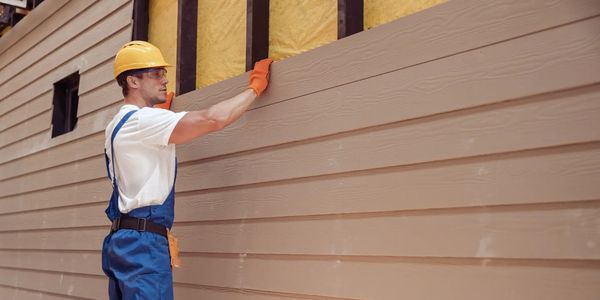 Worker installing tan vinyl siding on house