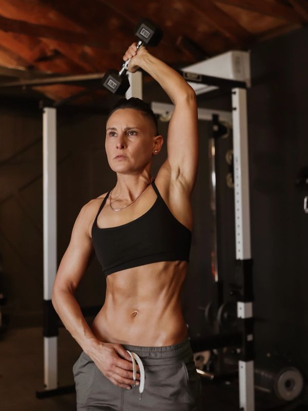 Woman lifting a dumbbell above her head in a gym.