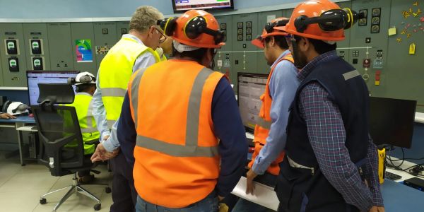 Engineers in safety gear monitoring control panels in an industrial control room.