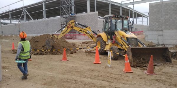 Construction site with a backhoe loader and a worker in safety gear.