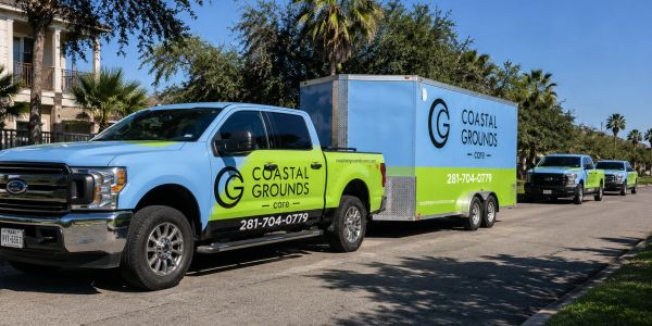 Coastal Grounds branded trucks and trailer parked on a sunny street.