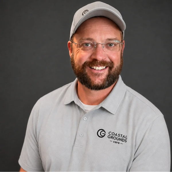 Smiling man in glasses and cap wearing a Coastal Grounds Care shirt.