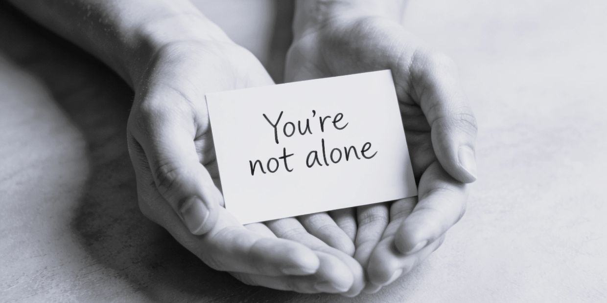 Hands holding a card with the message 'You're not alone.'