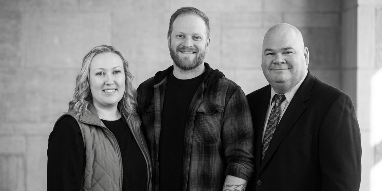 Three smiling adults posing together against a plain background.