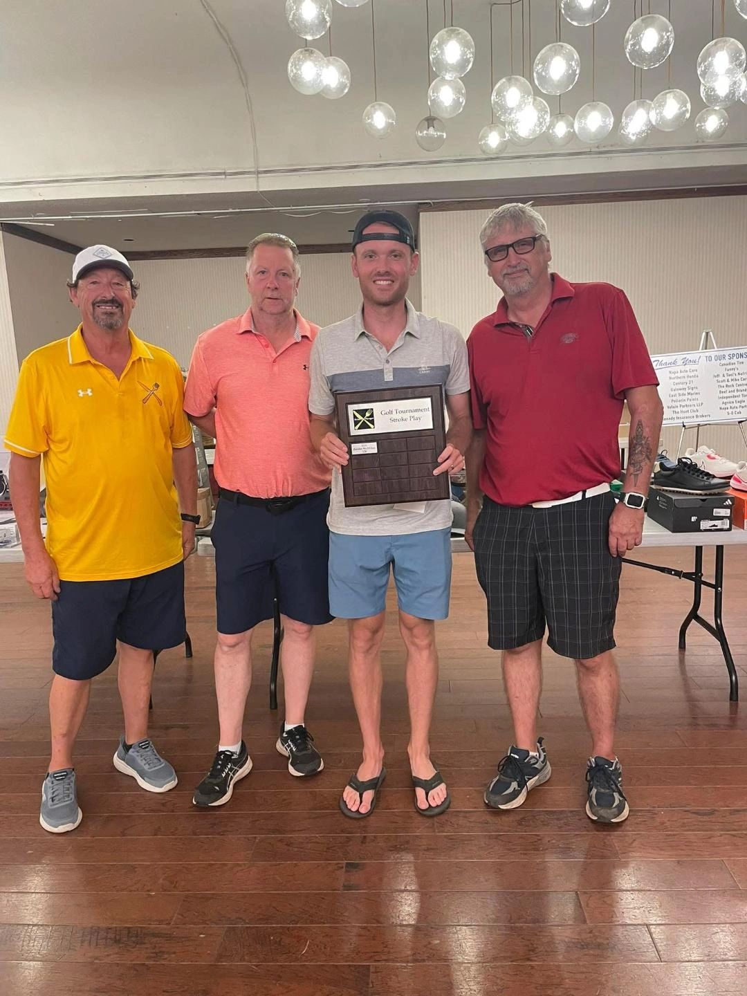 Four men standing indoors, one holding a golf tournament plaque.