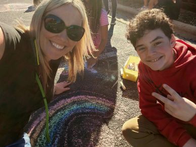 Two people smiling with chalk art rainbow on pavement.