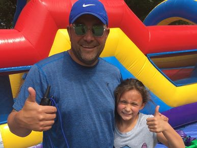 Man and child giving thumbs up in front of colorful inflatable.