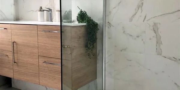Modern bathroom vanity with wood finish and marble wall.
