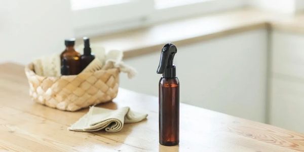 Amber spray bottle on a wooden table with a basket and cloth in the background.