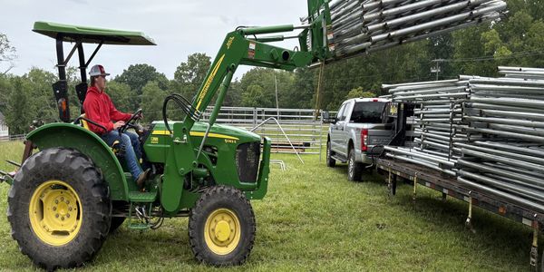 Man on green tractor lifting metal pipes.
