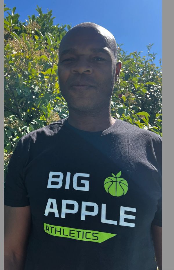 Man wearing a black 'Big Apple Athletics' t-shirt outdoors.