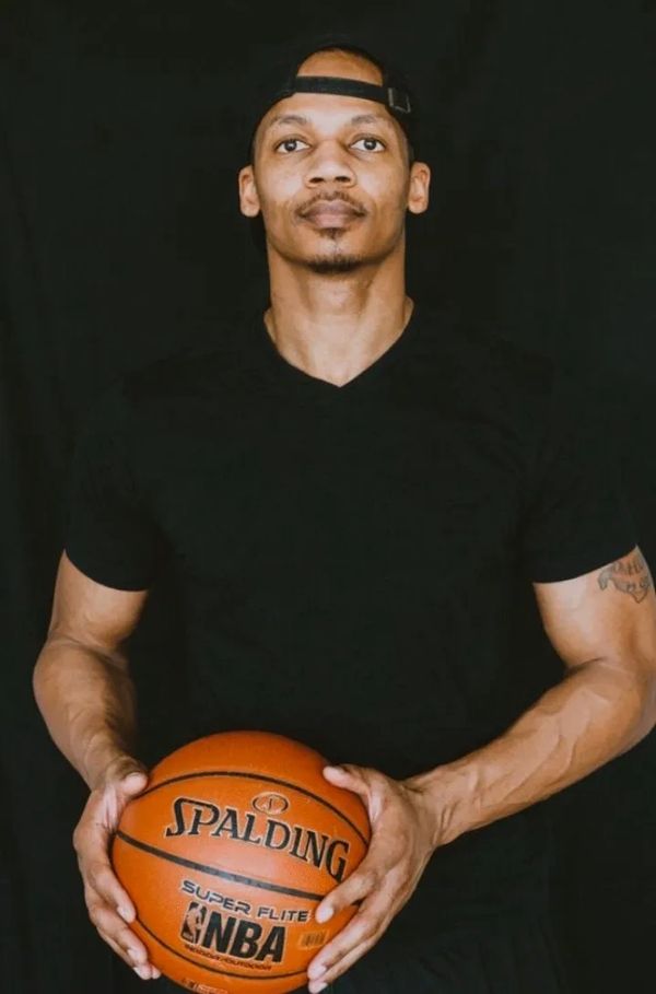 Man holding a basketball against a black background.