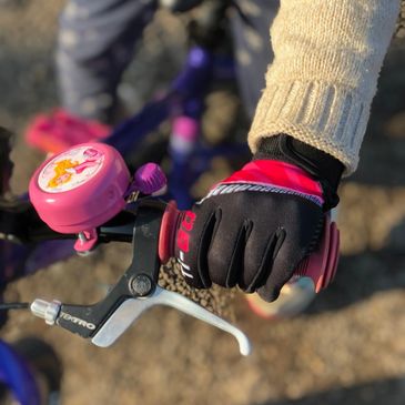 Child holding bike handlebar with pink Disney princess bellwearing Ti-Go Kids cycle gloves mitts