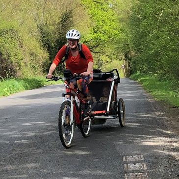 Mum woman cycling on road up hill with Thule Bike trailer and children on board smiling cycle helmet