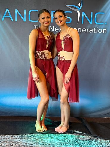 Two dancers in matching maroon costumes posing barefoot.