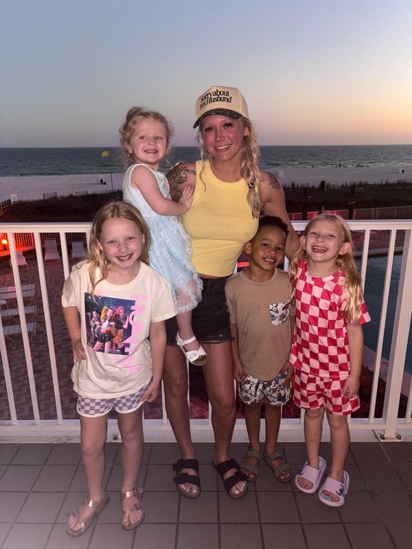 A woman with four smiling children on a balcony by the beach at sunset.