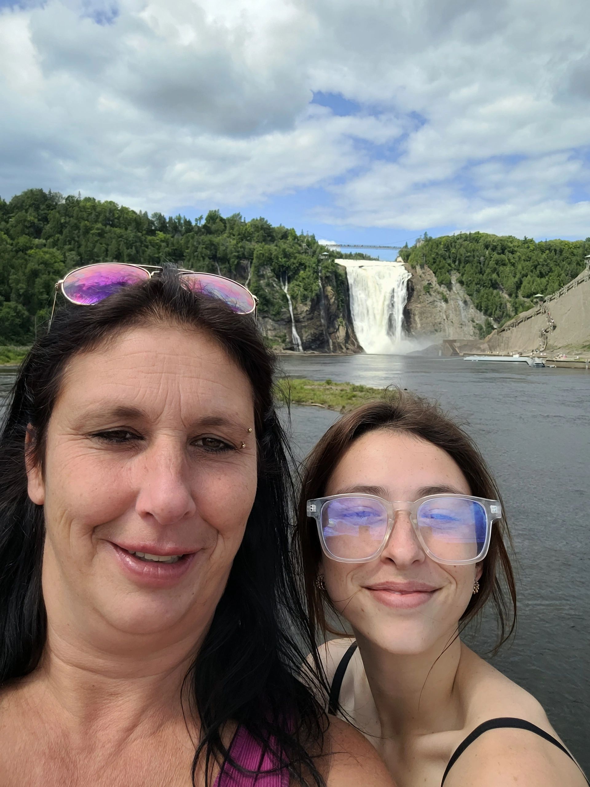 Two women smiling in front of a large waterfall and lush greenery.