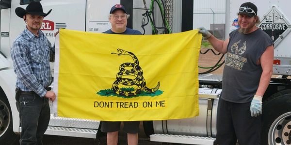 Three men holding a yellow "Don't Tread on Me" flag in front of a truck.