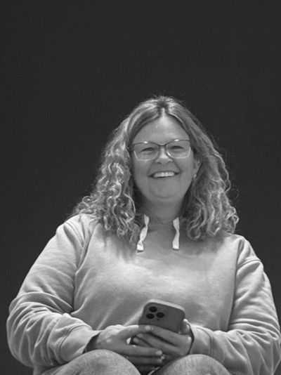 A smiling woman sits on carpeted stairs holding a phone indoors.