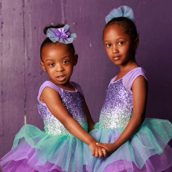 Two girls in matching purple and green tutus holding hands.