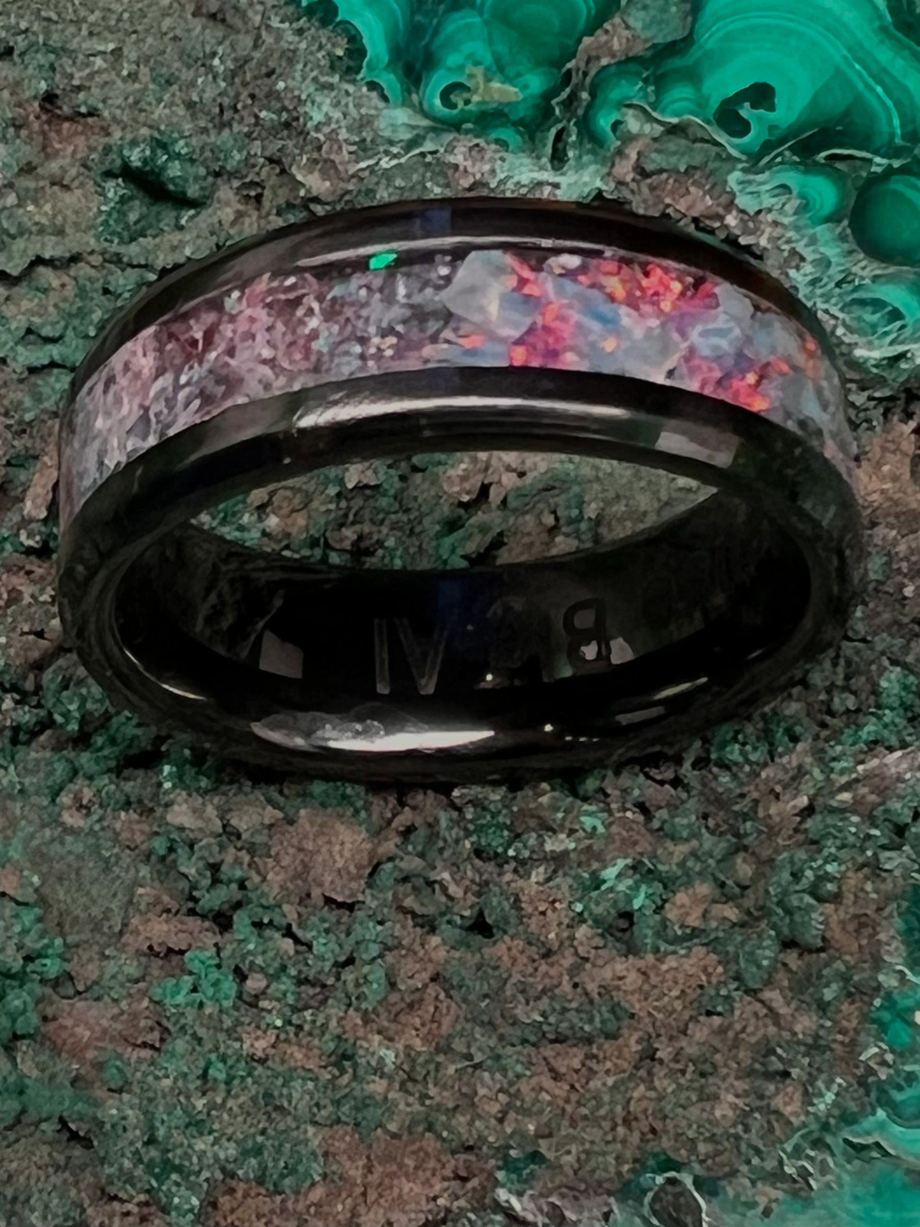 Black ring with colorful inlay on a textured green and brown surface.