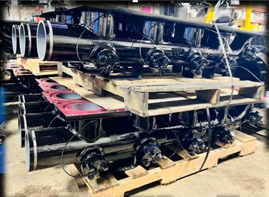 Stacked black industrial pipes on wooden pallets in a warehouse.