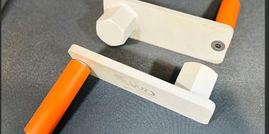 Two plastic clamps with orange handles on a gray surface.