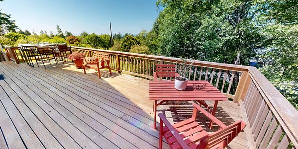 Spacious wooden deck with red chairs, tables, and lush green surroundings.