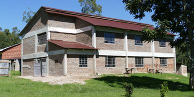 A large brick building with a red roof in a green yard under a clear sky.