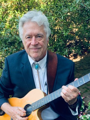 Older man playing acoustic guitar outdoors.