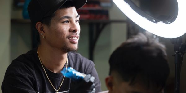 A man smiling while getting a tattoo under a ring light.