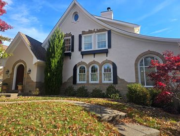 Charming house with arched windows, stone accents, and vibrant autumn foliage outside.