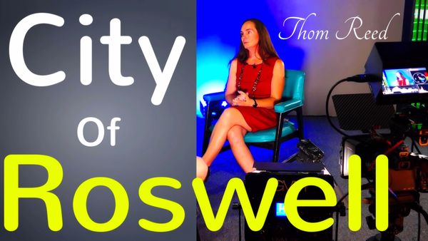 Woman in red dress seated for an interview with 'City of Roswell' text.