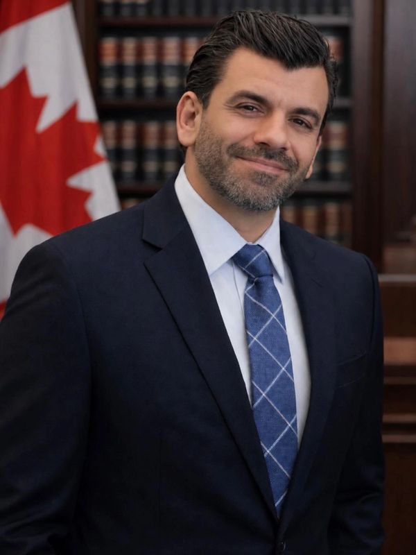 Man in suit with Canadian flag and bookshelves in background.