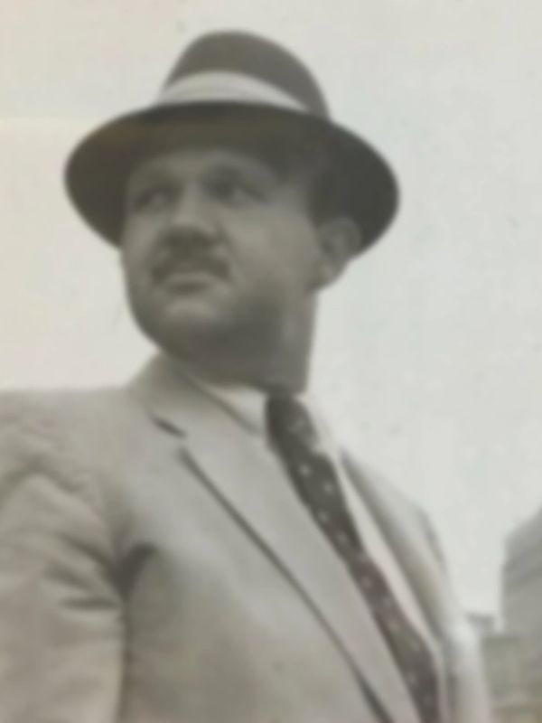 Sepia photo of iconic American advertising artist Saul Mandel in suit, tie, hat, & sky in background