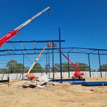 Construction site with cranes assembling a steel frame under clear blue sky.