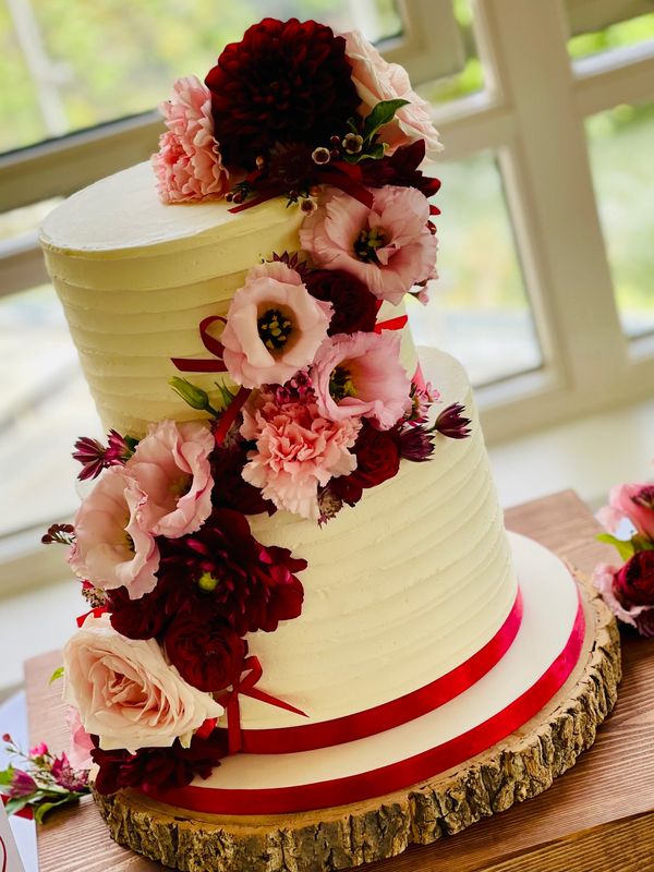 2 tier buttercream cake with pink and red flowers displayed on a hoop stand