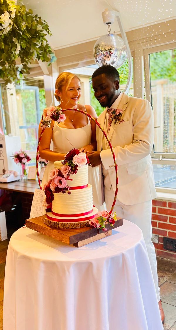 Bride & Groom cutting 2 tier buttercream cake with pink and red flowers displayed on a hoop stand