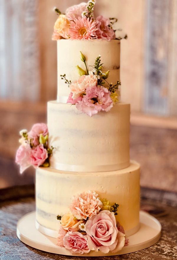 Pretty rustic 3 tier wedding cake on wine barrel in a pretty barn with fresh flowers pink tones