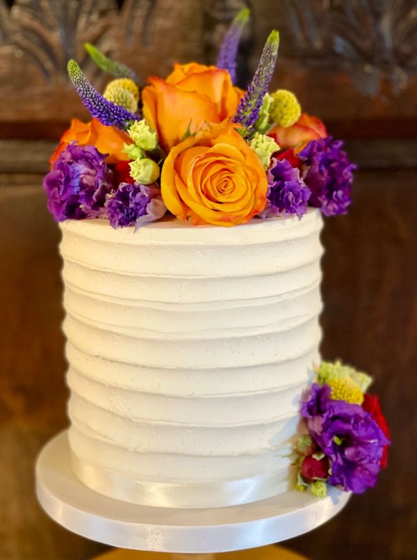 Small rustic  buttercream cutting cake with striking fresh flowers in shades of Orange, purple and r