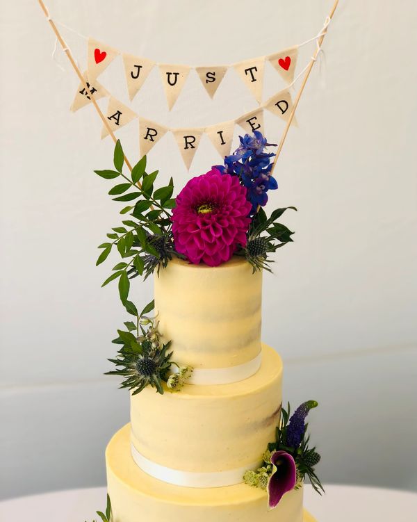 4 tier semi naked wedding cake with bright pink, blue, purple fresh flowers just married cake topper