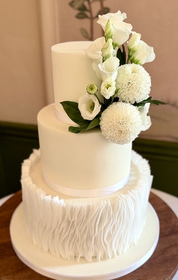 3 tier white fondant wedding cake with base of vertical wafer paper ruffles and fresh white flowers