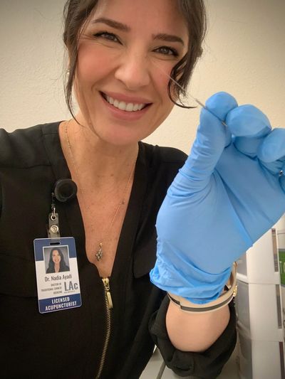 Smiling licensed acupuncturist holding an acupuncture needle with a gloved hand.