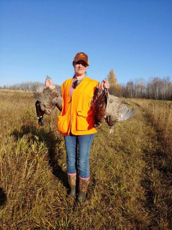 Woman hunter holding pheasants in a field.