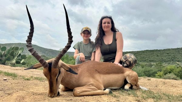 Two people posing with a large antelope outdoors.