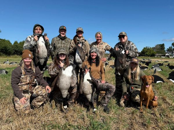 Group of hunters posing with geese and a dog.