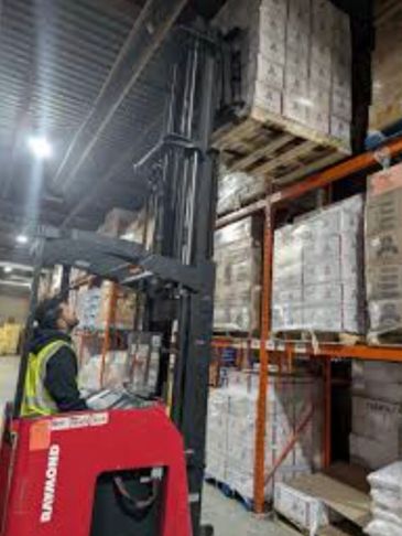 Worker operating a forklift to lift pallets in a warehouse.