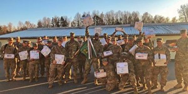 Group of soldiers in uniform holding certificates outside at sunset.