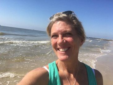 A woman smiling on a sunny beach with waves in the background.