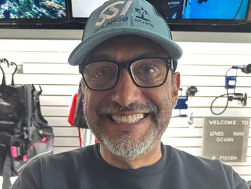 Smiling man wearing glasses and a cap in a scuba gear shop.